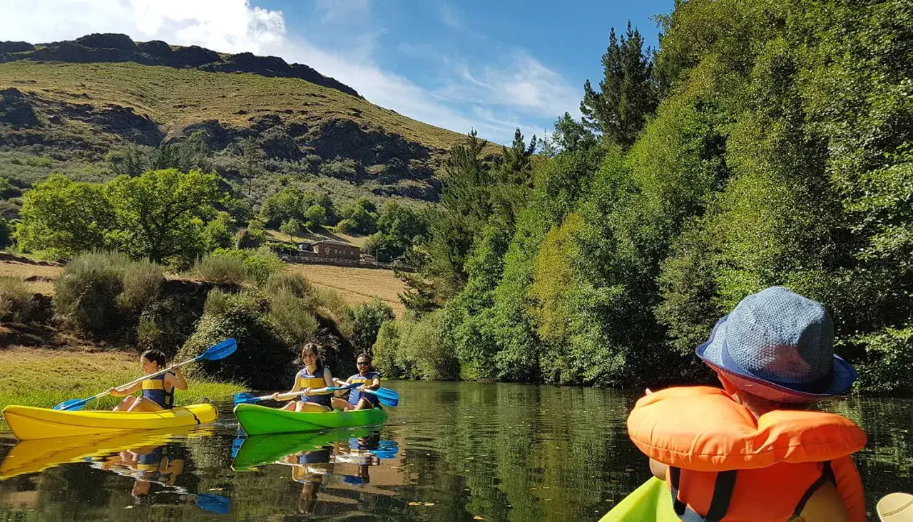 Disfrutando de un día de kayak en Asturias con niños. Paisaje verde y soleado, perfecto para aventuras familiares.