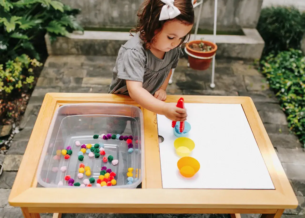 Niña de un año jugando con pompones y pinzas, una de las muchas actividades para niños de un año en guarderia.