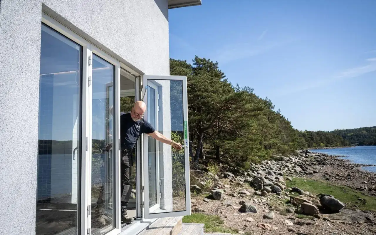 Man öppnar dörren till en modern stuga vid vattnet, med skog och klippor i bakgrunden. Hafsten stugor erbjuder en naturnära upplevelse.