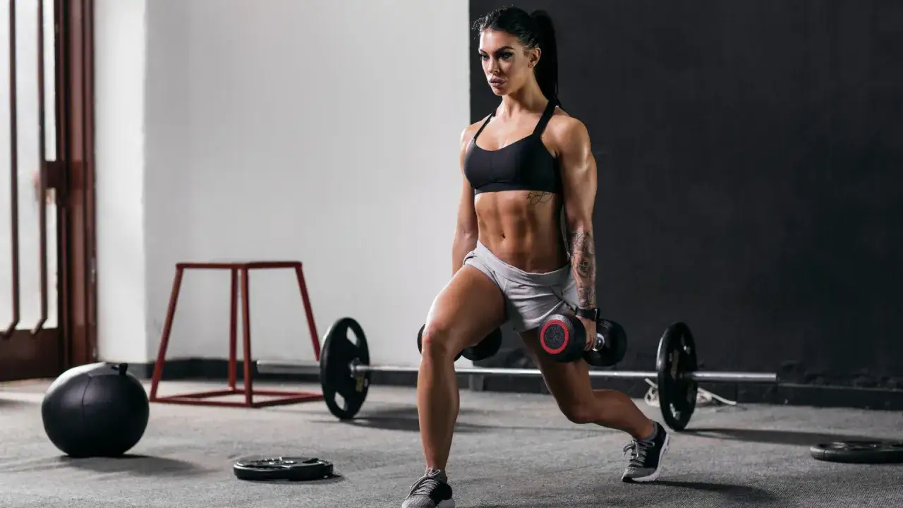 Donna muscolosa esegue affondi con manubri in palestra, un ottimo esercizio per come accelerare il metabolismo e tonificare il corpo.