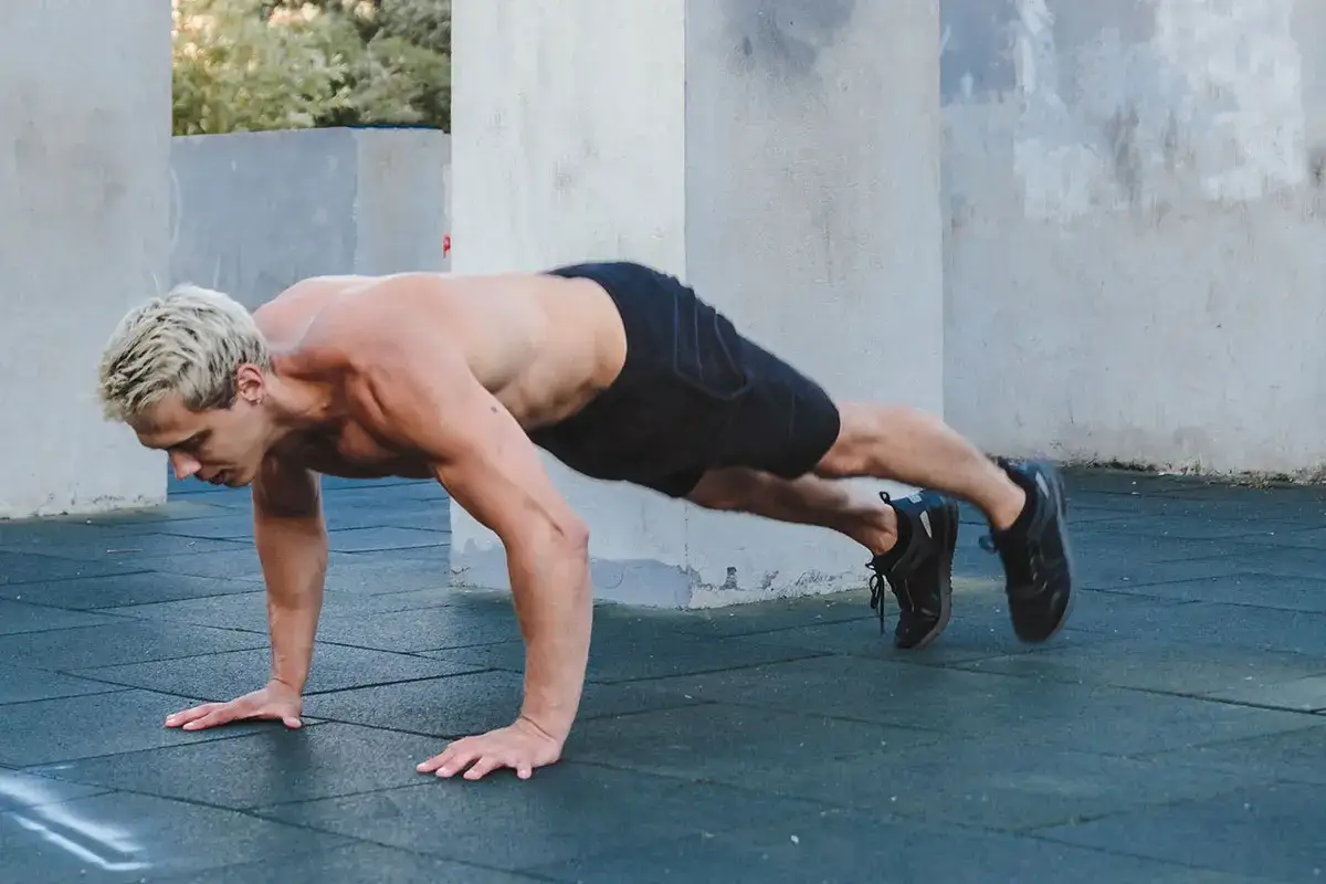 Mężczyzna wykonuje burpees po polsku, w pozycji deski na siłowni plenerowej.