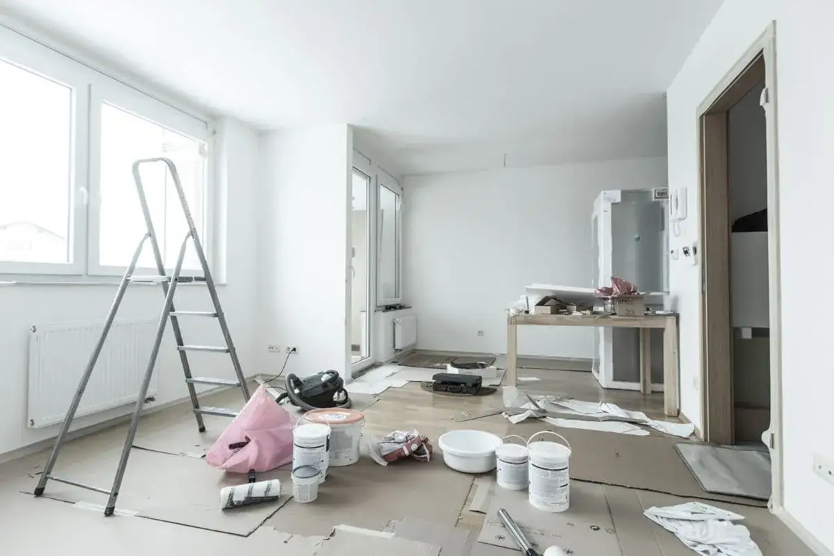 Habitación en reforma con escalera, cubos de pintura y aspiradora. Preparando la casa para mejorar la **eficiencia energética** y solicitar **deducciones IRPF**.