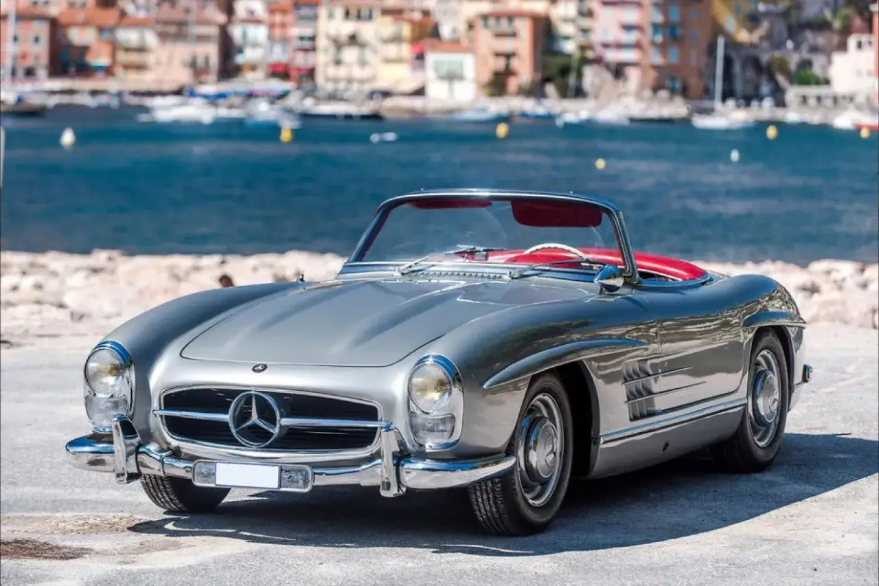 Srebrny Mercedes Gullwing z czerwonym wnętrzem na tle zatoki z łodziami. Ikona motoryzacji.