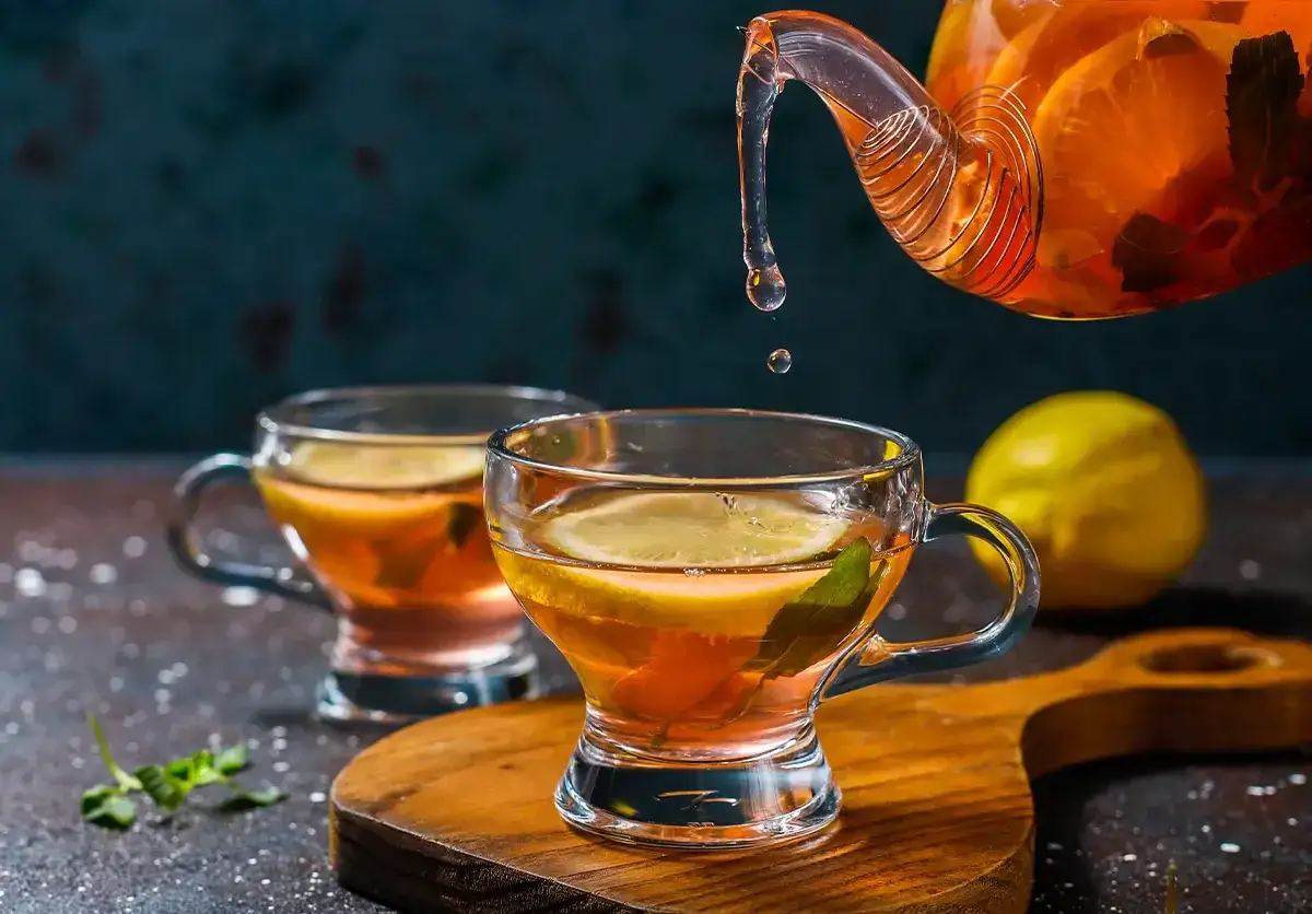 Gorąca herbata z cytryną i miętą, idealna na chłodne dni. W tle dzbanek z aromatycznym napojem, przypominającym masala chai.