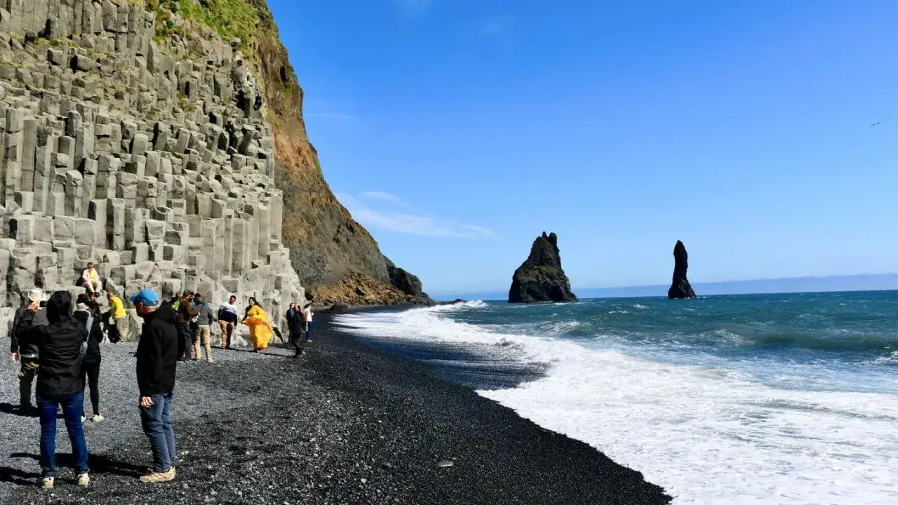 Besökare beundrar de unika basaltpelarna och den dramatiska svarta sanden vid Reynisfjara.