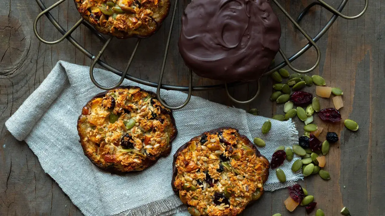 Frukostkakor med nötter, frön och torkad frukt, perfekta att baka utan socker. En chokladöverdragen kaka ligger bredvid.