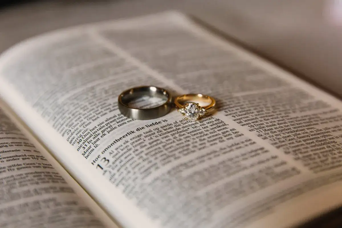 Dwie obrączki na otwartej Biblii, symbolizujące miłość małżeńską i cytaty z Biblii o miłości małżeńskiej.