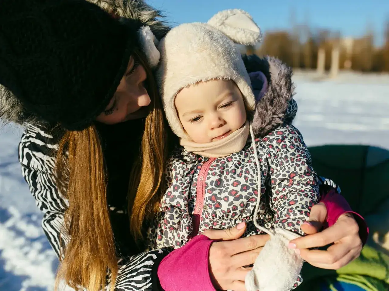 Mama tuli dziecko do nosidełka zimą. Ciepło ubrane, w futrzanych czapkach, gotowe na spacer.