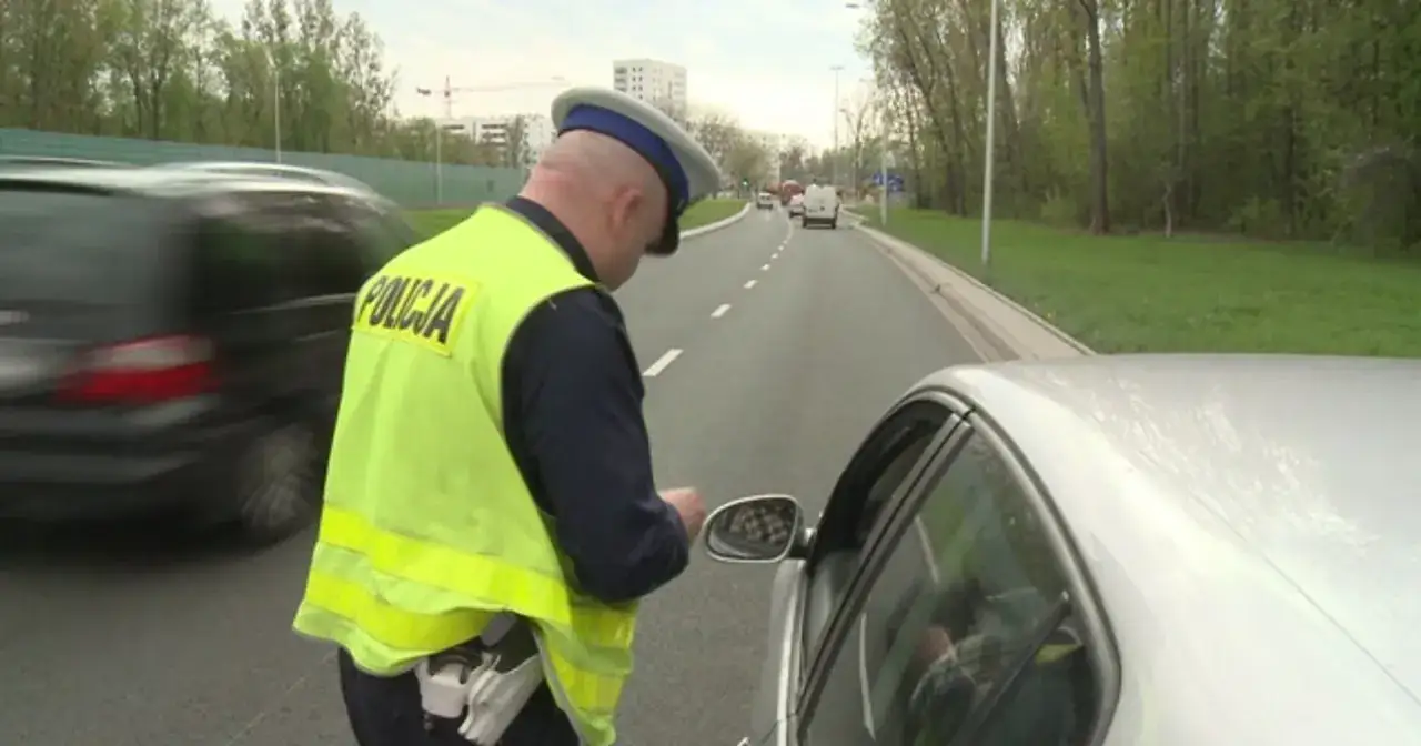 Policjant w kamizelce odblaskowej spisuje kierowcę. Może to być mandat za brak prawa jazdy.