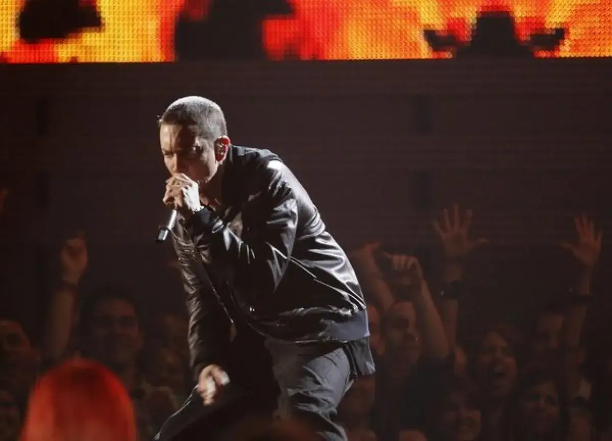 Eminem, znany z tego, jak ma na imię, występuje na scenie w sk&oacute;rzanej kurtce, śpiewając do mikrofonu. Tłum wiwatuje.