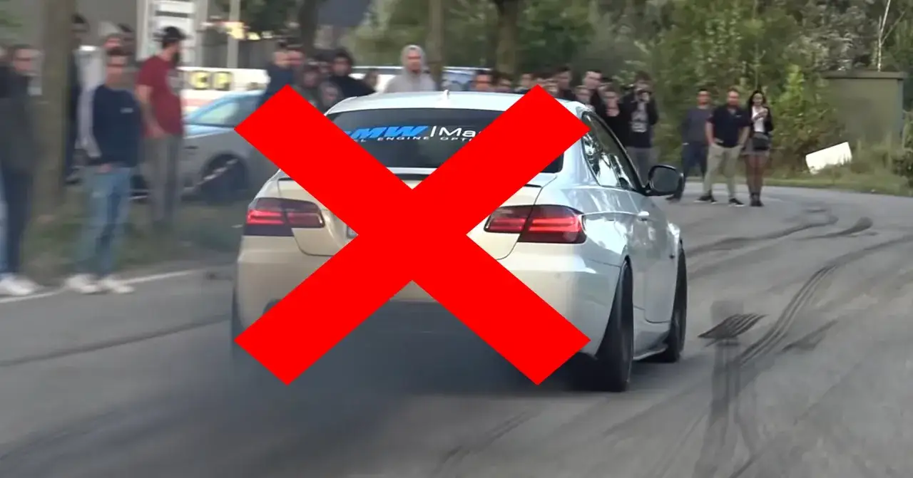 Widok z tyłu białego BMW z dymem z opon i dużym czerwonym krzyżem. To przyszłość bez samochodów spalinowych.