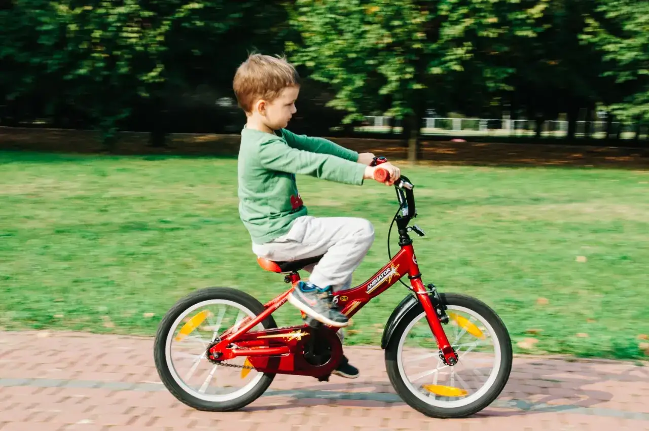 Chłopiec z radością pedałuje na czerwonym rowerku po parku. Od kiedy rowerek z pedałami, świat stał się jego placem zabaw.