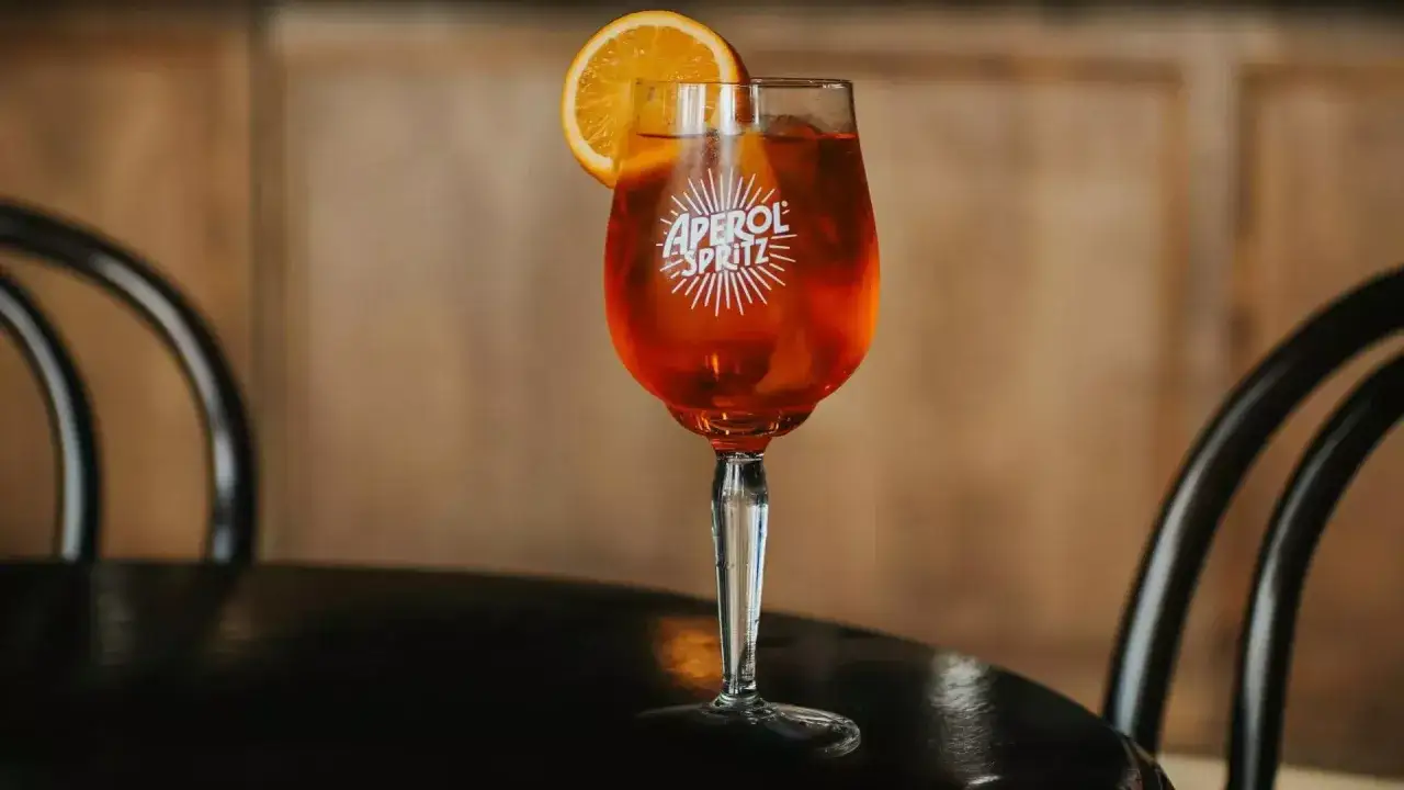 Orzeźwiający aperol z tonikiem, ozdobiony plasterkiem pomarańczy, czeka na stoliku. Idealny na letnie popołudnie.