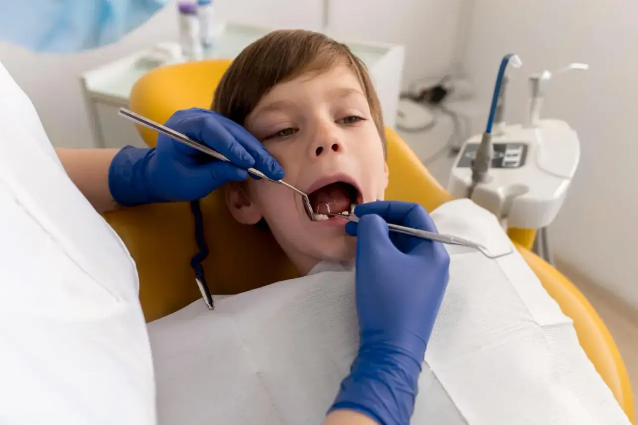 Chłopiec przechodzi leczenie kanałowe u dzieci. Dentysta w niebieskich rękawiczkach bada jego ząb.