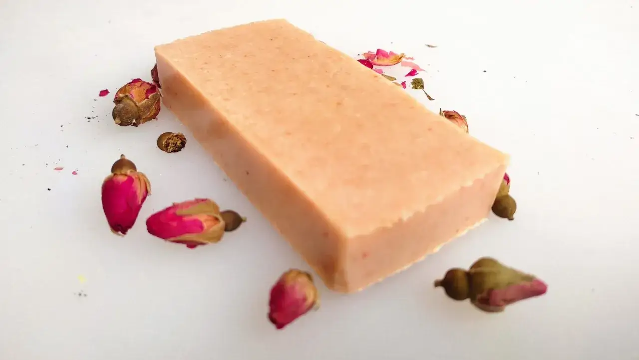 Un sapone artigianale color pesca, circondato da boccioli di rosa secchi. Un'idea di come è fatto il sapone con ingredienti naturali.