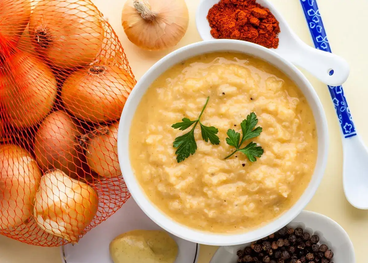 Un taz&oacute;n de cremosa salsa de cebolla, decorado con perejil, junto a cebollas frescas, piment&oacute;n y granos de pimienta.