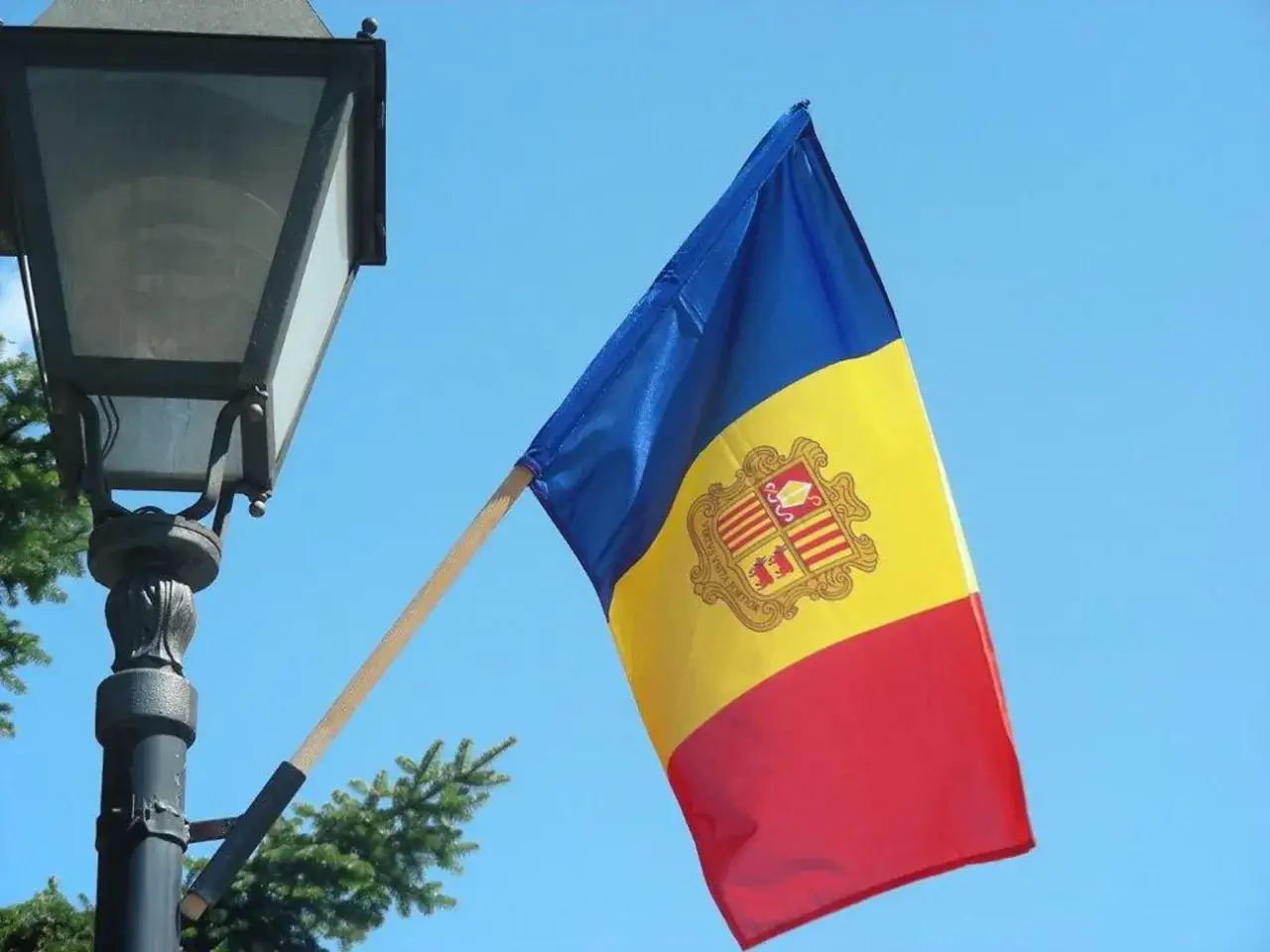 Flaga Andory, kraju graniczącego z Francją i Hiszpanią, powiewa na tle błękitnego nieba obok latarni.