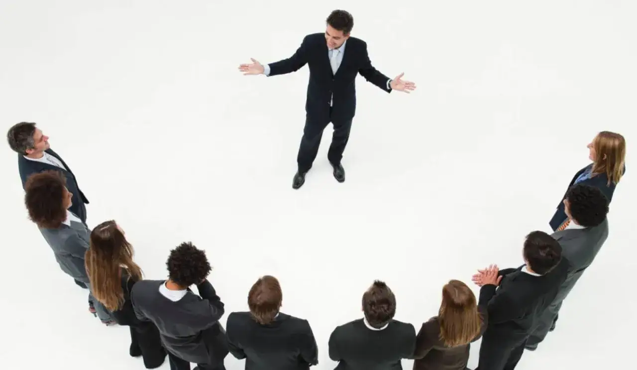 Un l&iacute;der inspira a su equipo. Un grupo de personas en c&iacute;rculo escuchan atentamente a un hombre que demuestra master liderazgo y gesti&oacute;n de equipos.