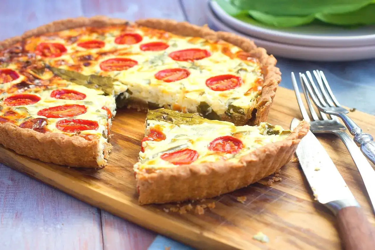 Herzhafte Quiche mit Tomaten und grünem Gemüse, perfekt für leckere Quiche Rezepte. Ein Stück wurde bereits entnommen.