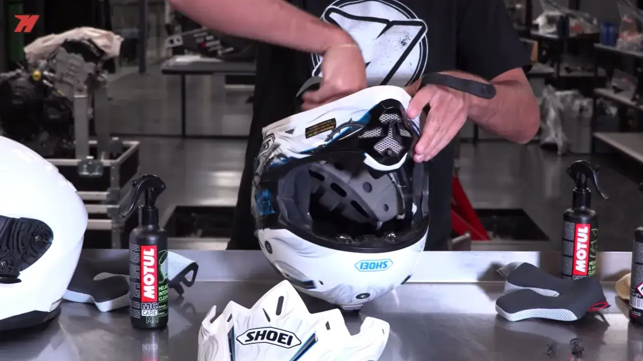 Hombre limpiando el interior de un casco de moto con un spray. No es un lavavajillas, sino un limpiador específico para cascos.