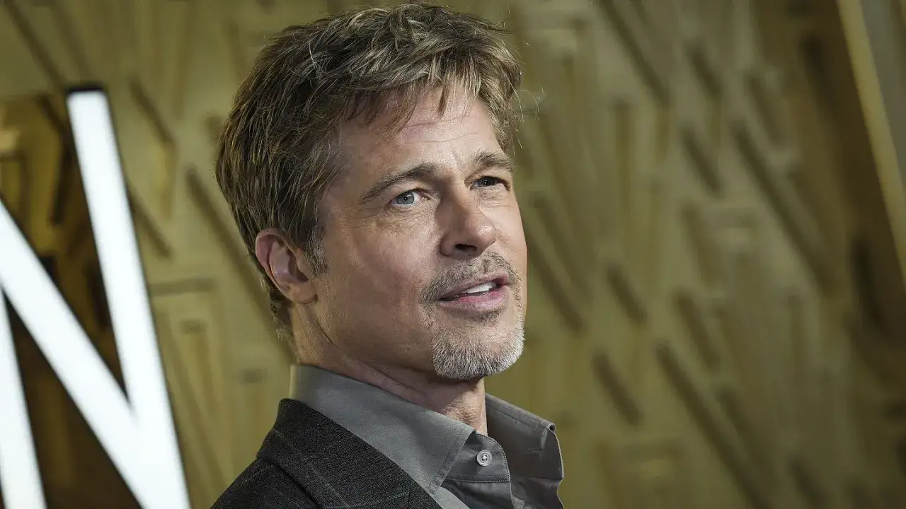 Brad Pitt, którego wiek widać po siwych włosach i zmarszczkach, w eleganckim garniturze.