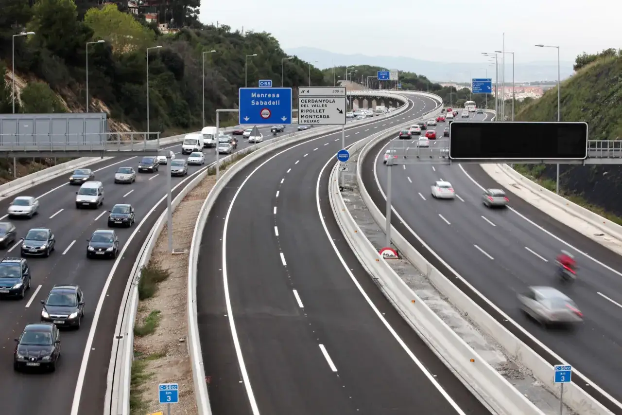 Tráfico en la autopista C-58, vía de acceso a vao Barcelona. Coches y furgonetas circulan por carriles amplios rodeados de vegetación.