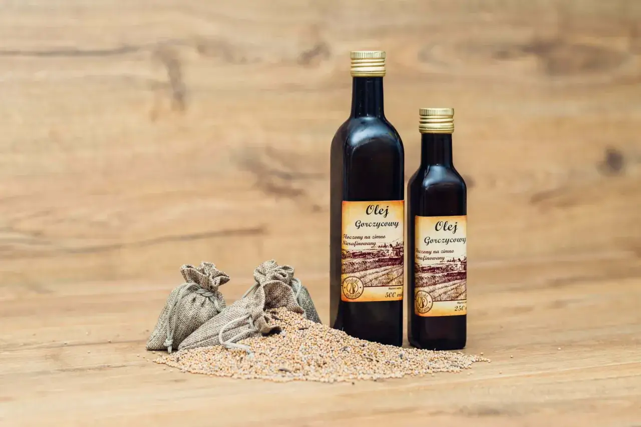 Olej z gorczycy w ciemnych butelkach, obok woreczków z nasionami gorczycy. Naturalny produkt.