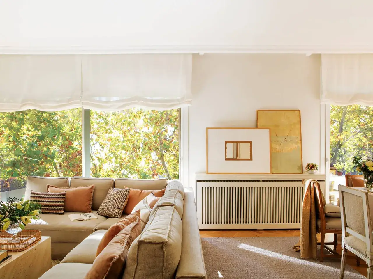 Un cómodo sofá beige con cojines de colores, junto a una ventana con vistas a árboles frondosos.