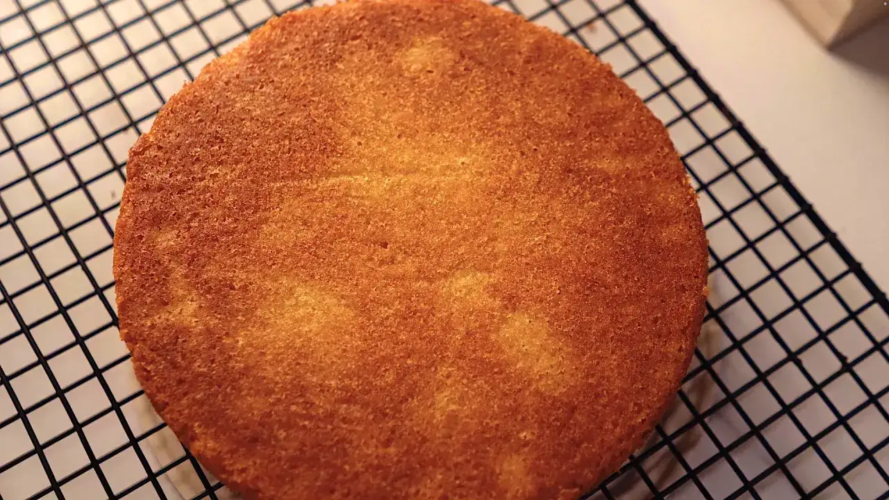 Gâteau génoise doré, tout juste sorti du four, refroidissant sur une grille. La cuisson est parfaite.