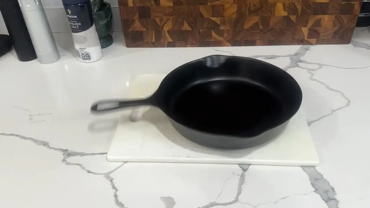 Poêle en fonte noire sur une planche à découper blanche, prête à redresser le fond.