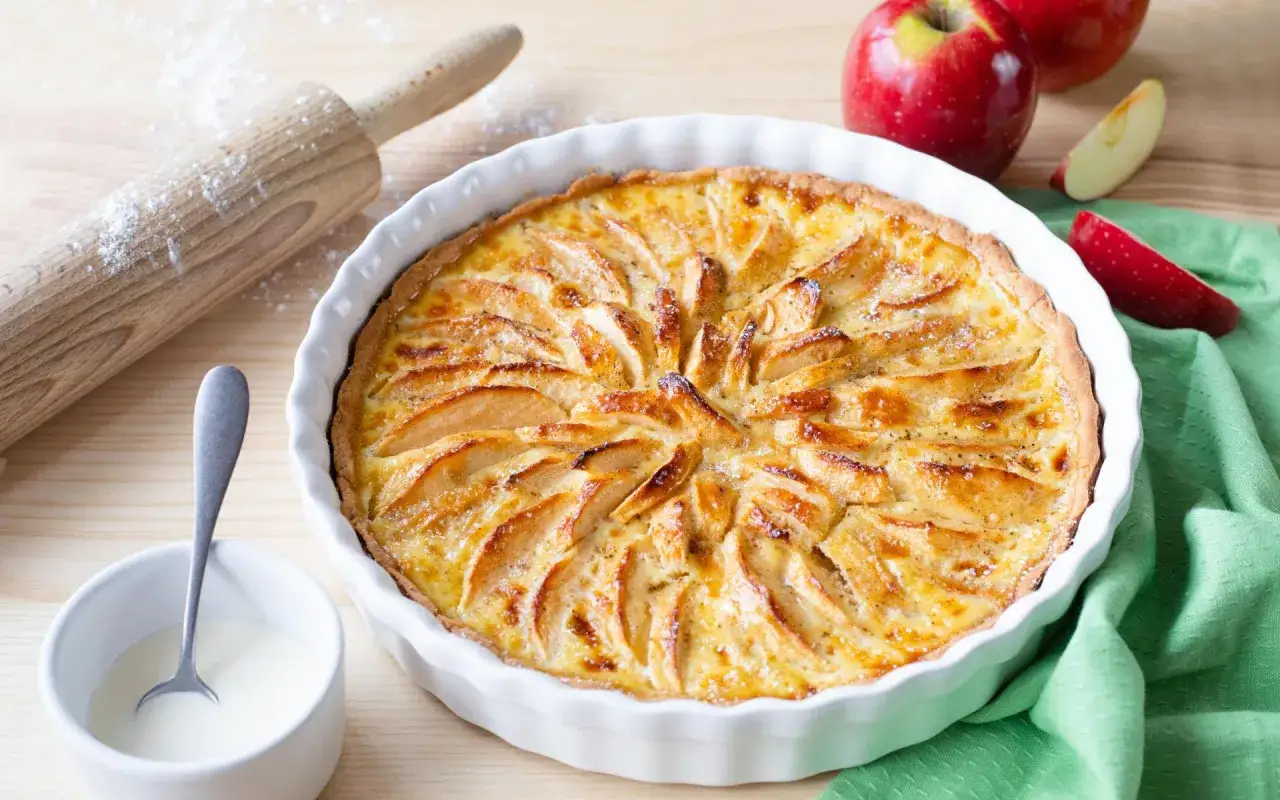 Tarte normande aux pommes dorée et appétissante, prête à être dégustée. Des pommes caramélisées sur une crème onctueuse.