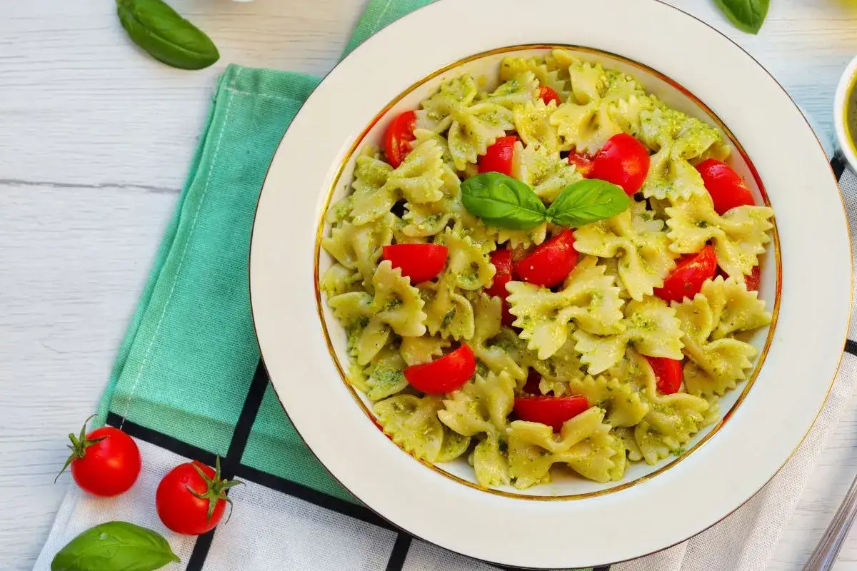 Farfalle condite con pesto fresco e pomodorini, un piatto estivo di pasta alla crudaiola, guarnito con basilico.