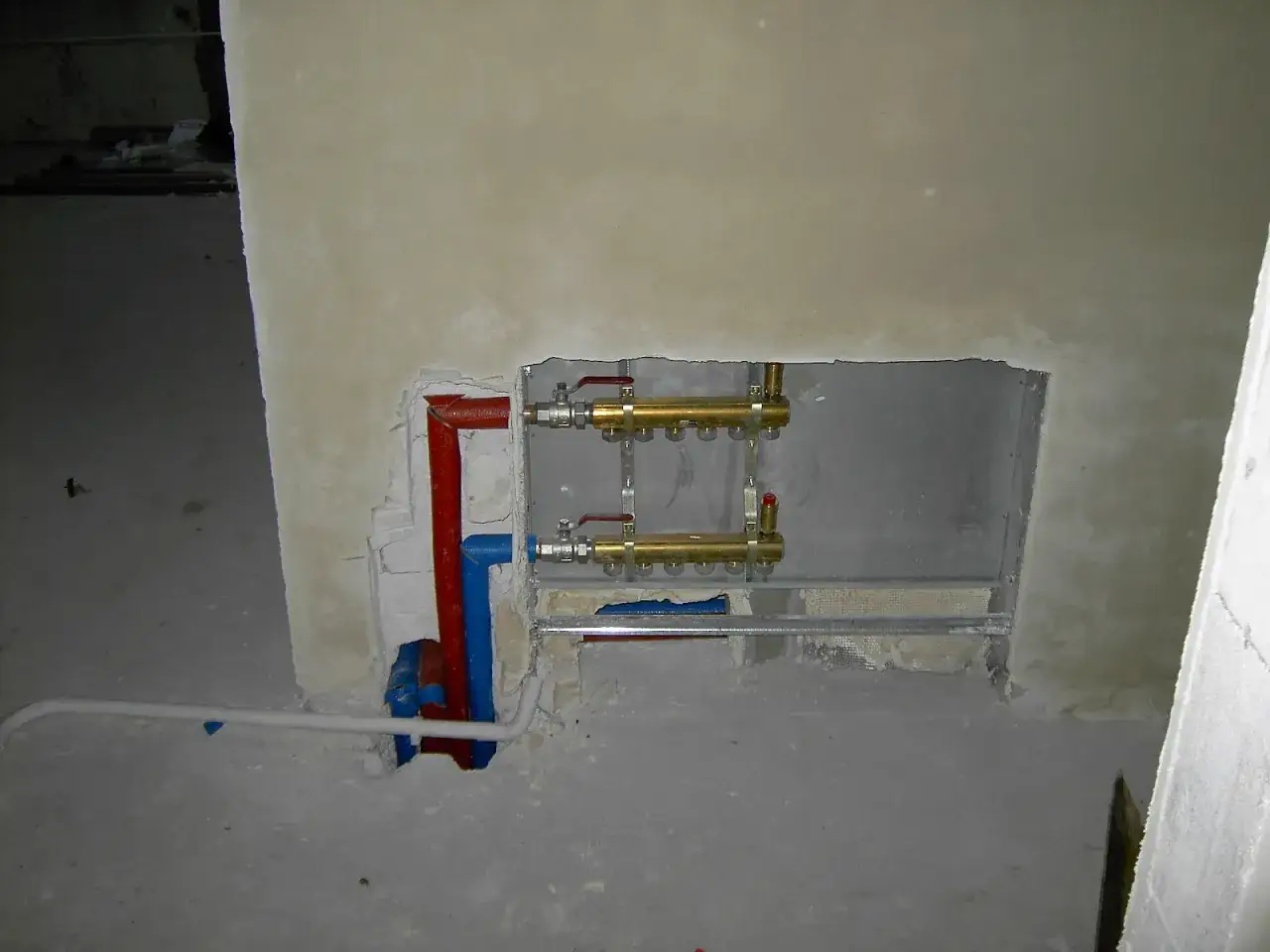 Instalacja hydrauliczna przed tynkami: miedziane rozdzielacze i rury w ścianie.