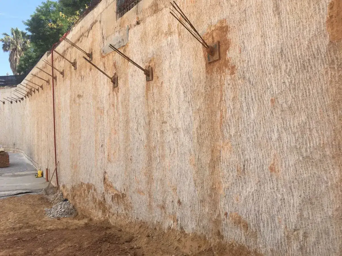 Muros pantalla de contenci&oacute;n en proceso de construcci&oacute;n, con anclajes met&aacute;licos y textura rugosa.