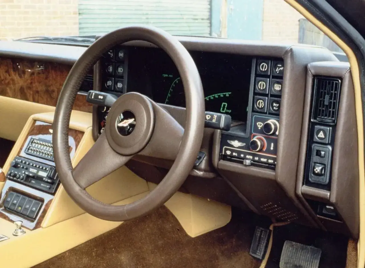 Interiör i en Aston Martin Lagonda med trädetaljer, digital instrumentpanel och klassisk ratt.