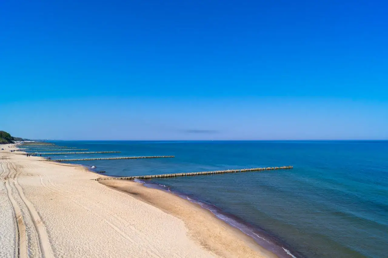 Piękna plaża i spokojne morze na zachodniopomorskich miejscowościach nadmorskich. Drewniane falochrony tworzą rytmiczne linie w wodzie.