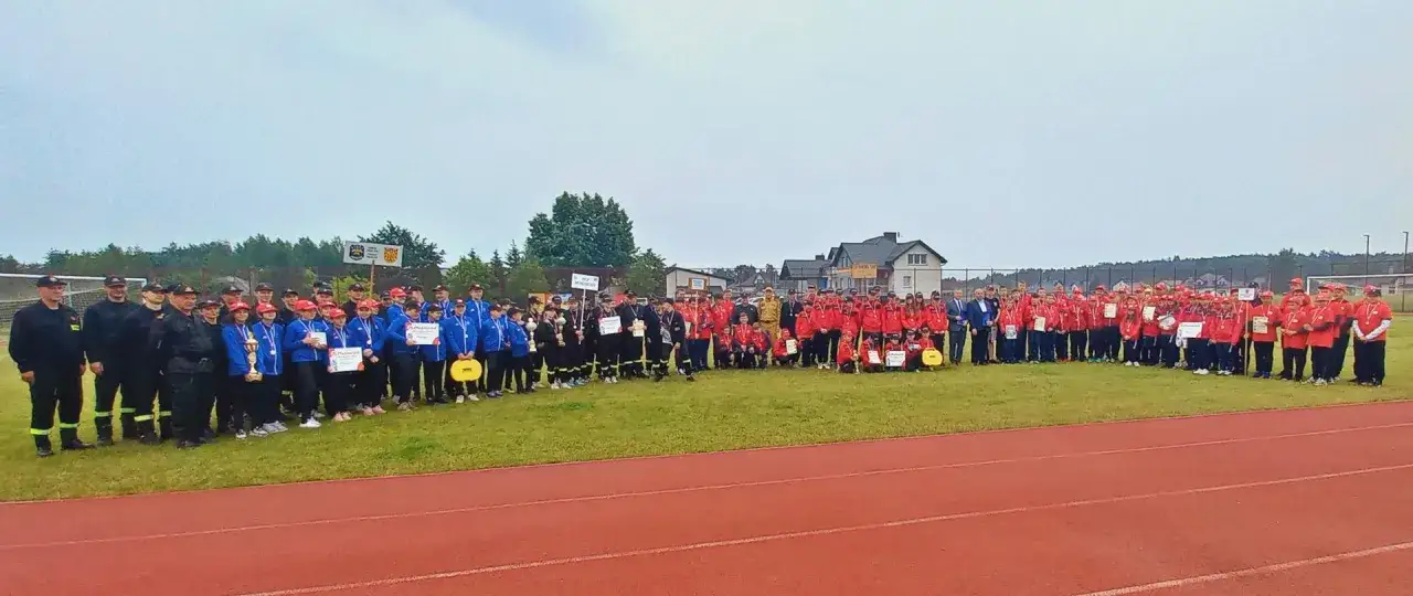 Uczestnicy zawodów CTIF, w tym strażacy i młodzież, pozują do wspólnego zdjęcia z pucharami i medalami.