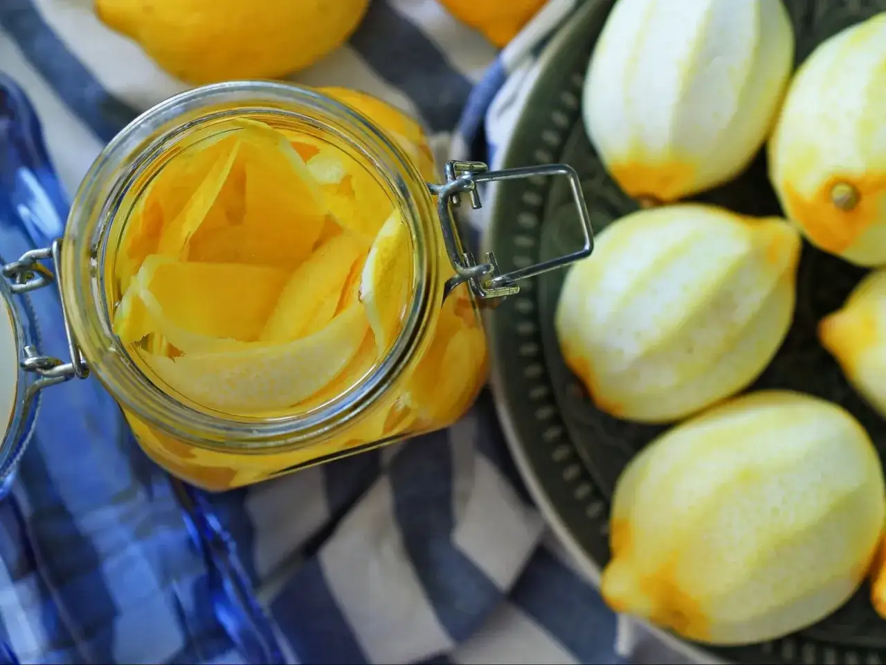 Skórki cytryn w słoiku, gotowe na przepis na limoncello. Obok świeże cytryny na talerzu.