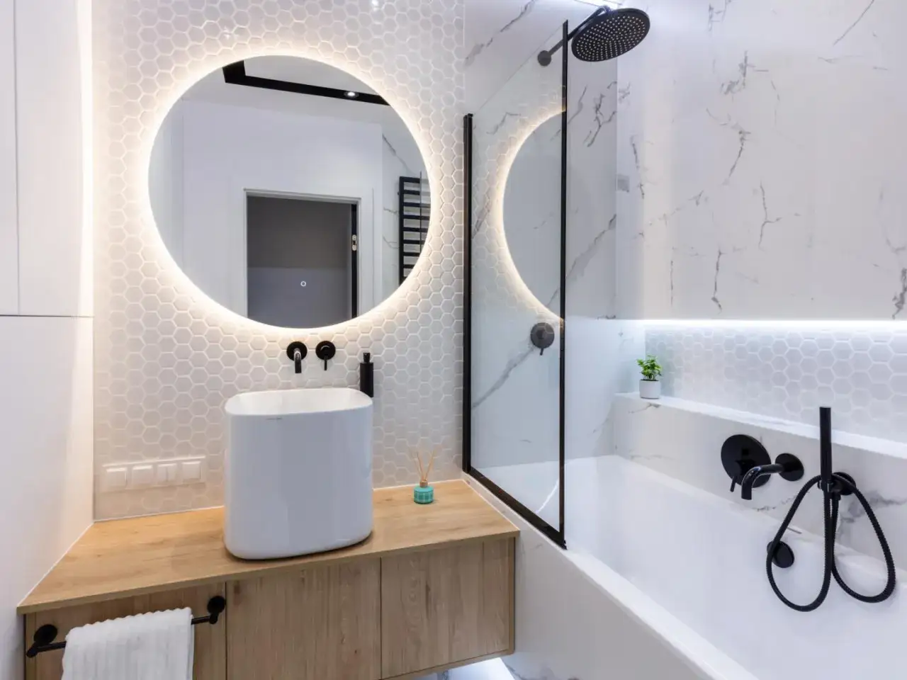 Moderno bagno con lavabo bianco su mobile in legno, specchio rotondo illuminato e vasca con doccia. Idee per un bagno cieco.