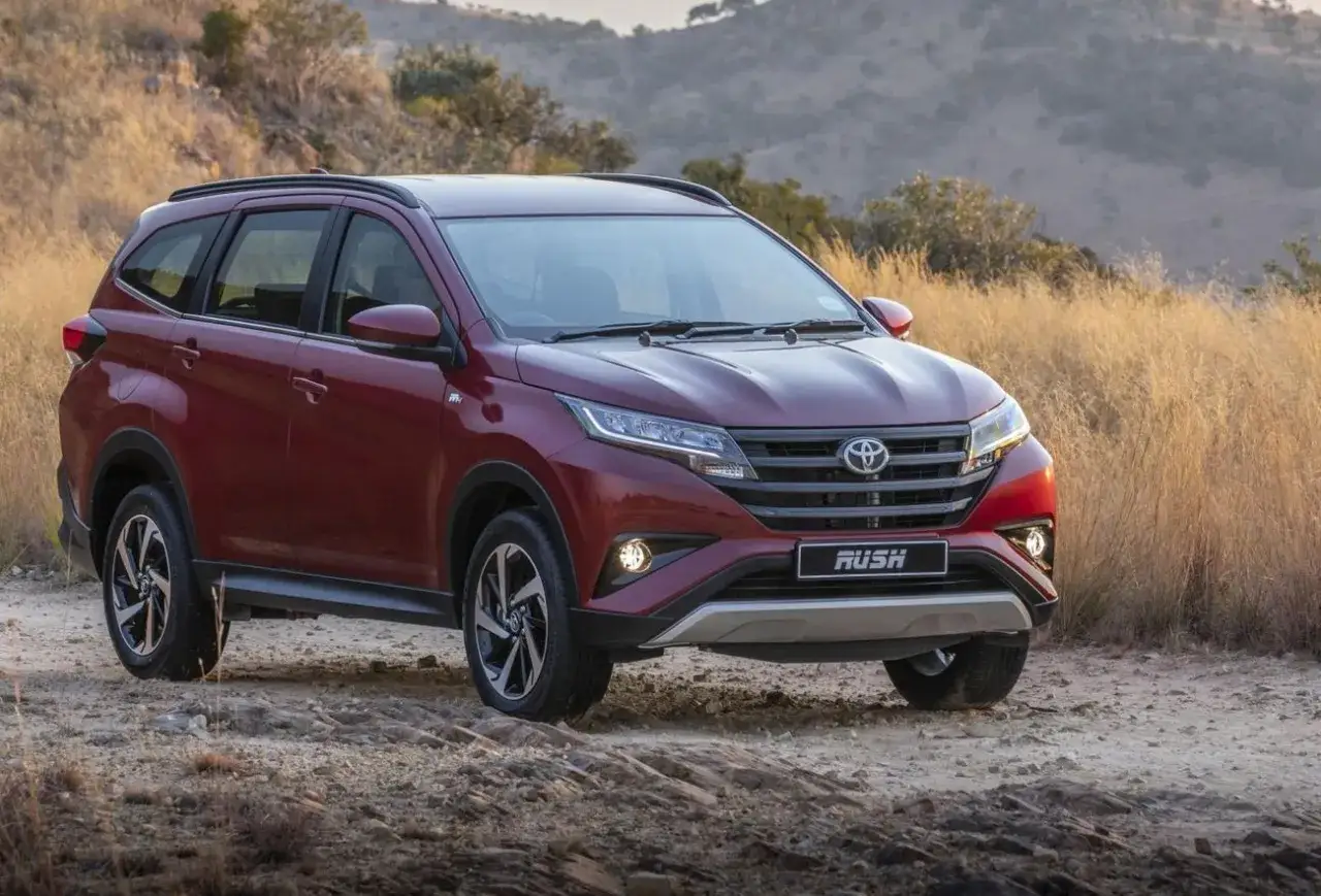 Czerwony Toyota Rush na drodze gruntowej, otoczony suchą trawą i krzewami.