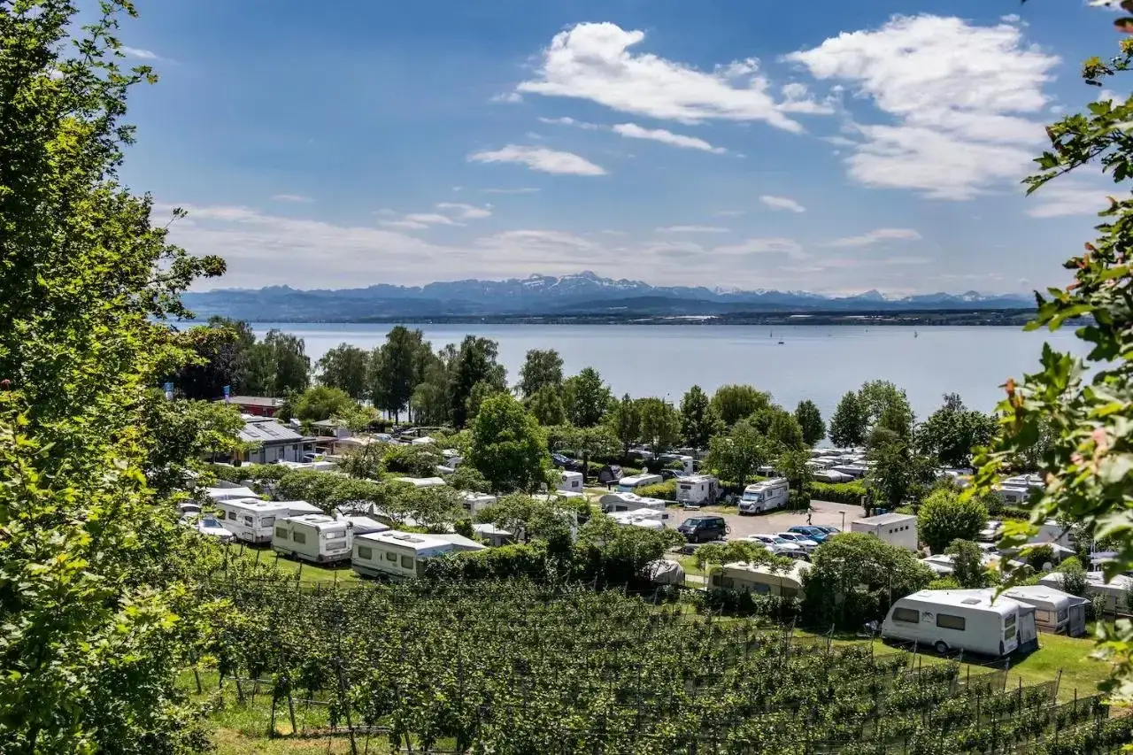 Wohnmobile und Wohnwagen auf einem Campingplatz mit Blick auf den Bodensee und die Alpen. Die Hagnau Promenade ist in der N&auml;he.