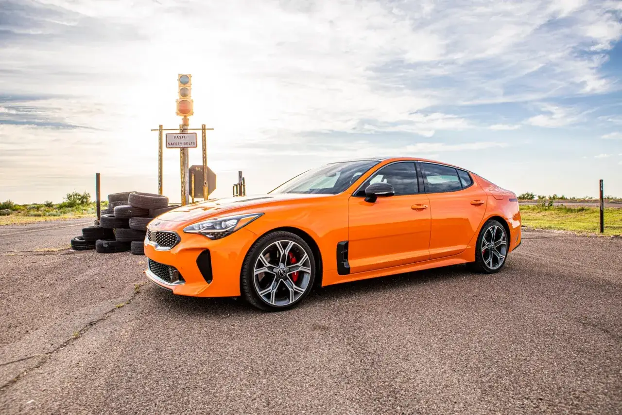 Pomarańczowy Kia Stinger GT stoi obok stosu opon i sygnalizacji świetlnej na pustkowiu.