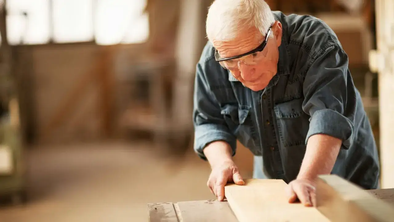 Hombre mayor con gafas de seguridad trabajando la madera, ejemplo de jubilación activa.