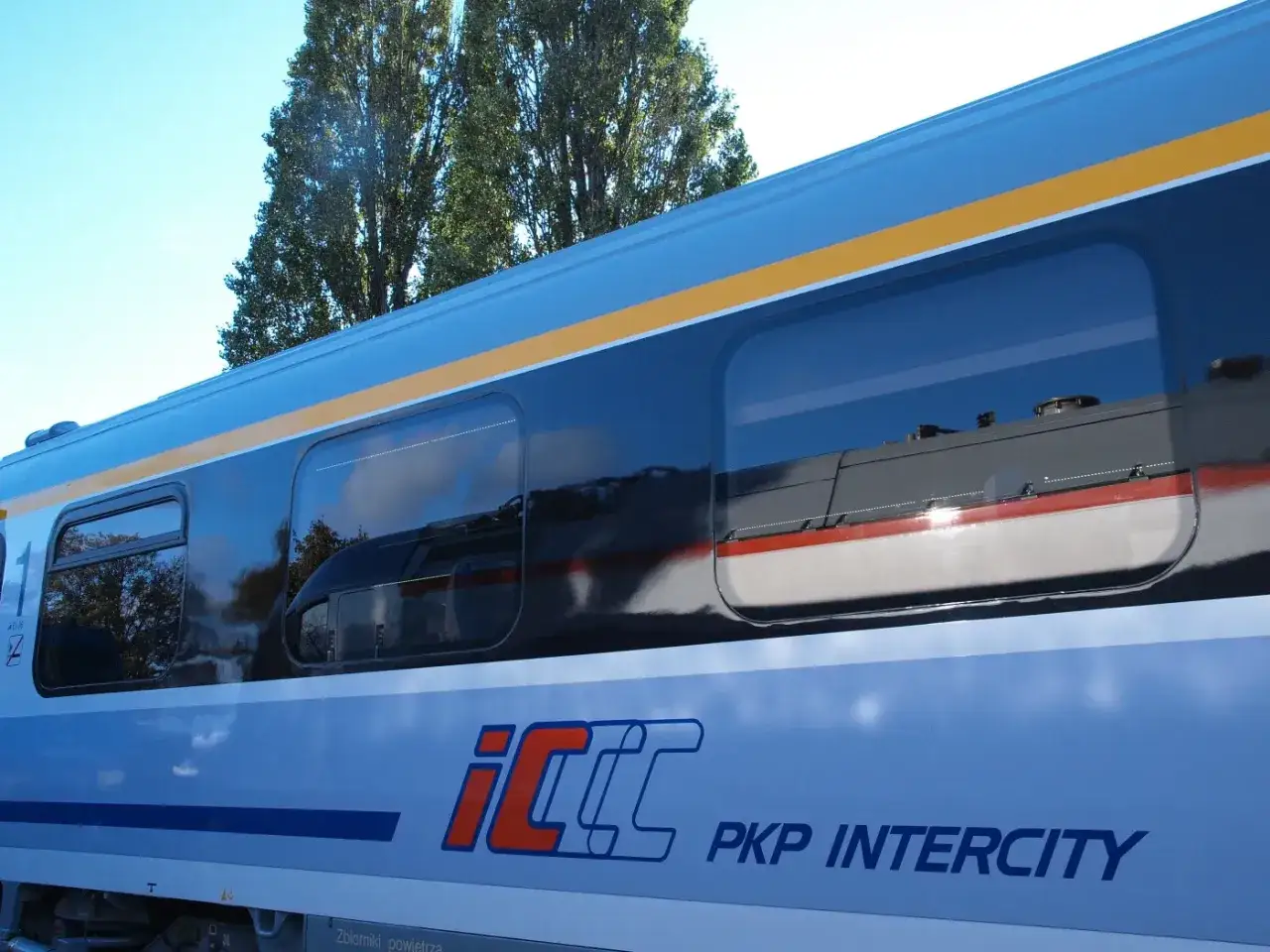 Boczna ściana pociągu Pendolino PKP Intercity z odbiciem drzew w oknach. Może to być widok podczas podróży lub przed zwrotem biletu Pendolino.