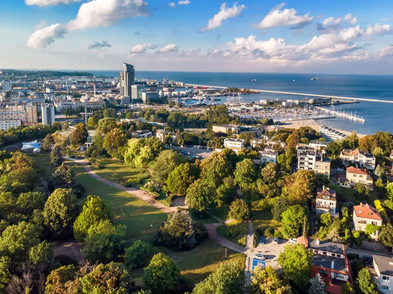 Vacker utsikt &ouml;ver Gdynia, Polen, med en gr&ouml;nskande park i f&ouml;rgrunden och en livlig hamn vid &Ouml;stersj&ouml;n.