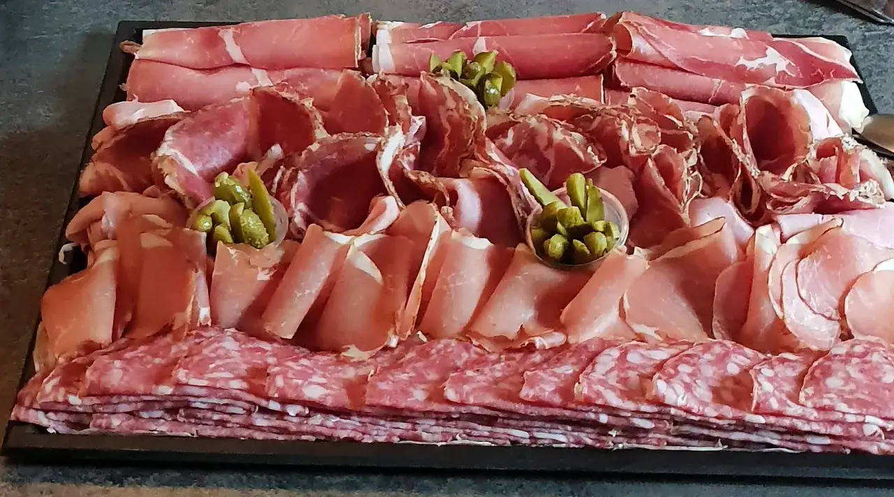 Plateau de charcuterie variée, avec du jambon cru, du saucisson et des cornichons, parfait pour un apéritif raclette.