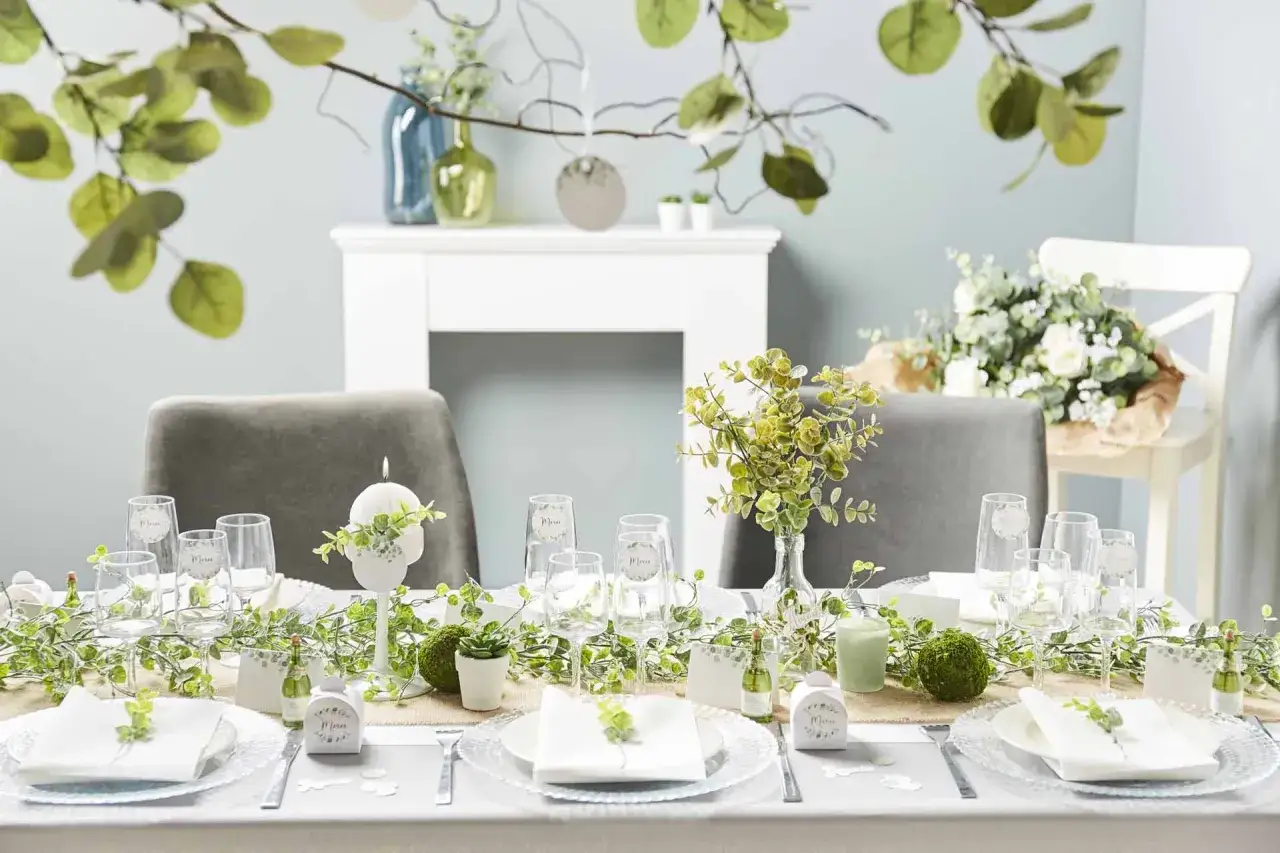 Une table joliment dressée pour organiser un baptême chez soi. Décoration champêtre avec guirlandes de verdure, bougies et petites attentions.