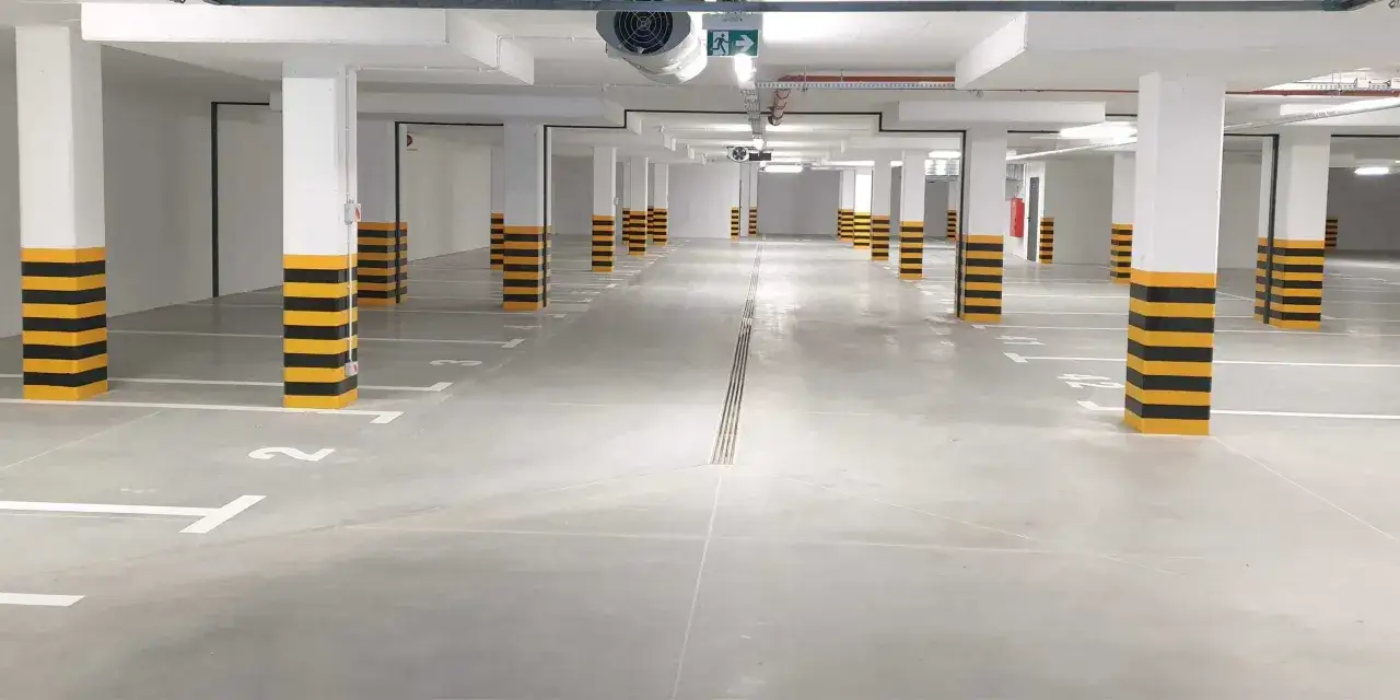 Puste miejsce postojowe w podziemnym garażu. Słupy pomalowane na żółto-czarne pasy.