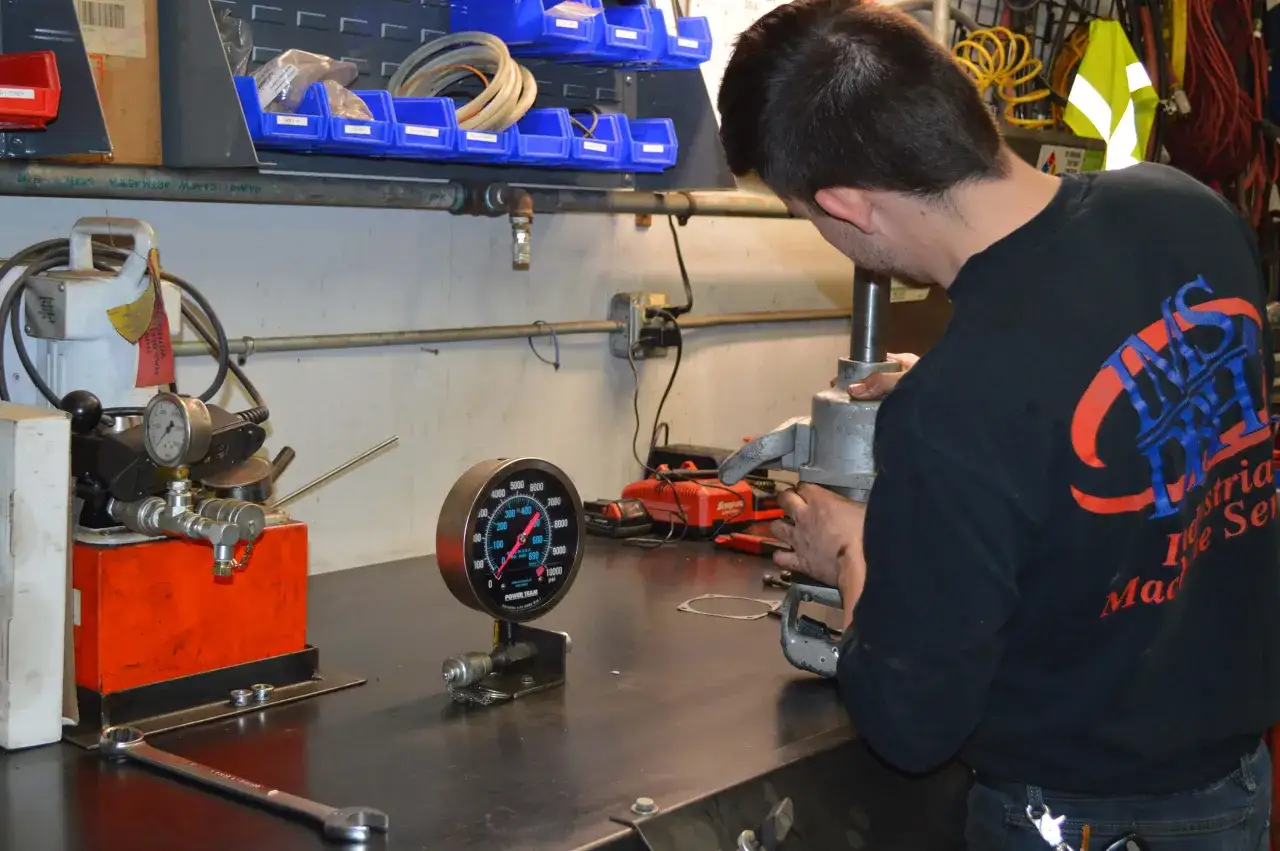 Mechanik pracuje nad regeneracją siłownik&oacute;w pneumatycznych, używając manometru do kontroli ciśnienia.