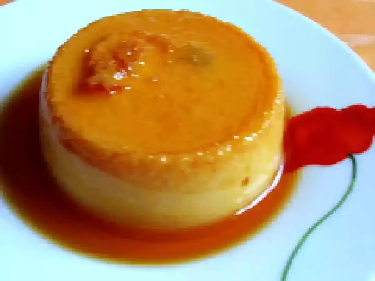 Un d&eacute;licieux g&acirc;teau de semoule napp&eacute; de caramel ambr&eacute;, servi sur une assiette orn&eacute;e d'un coquelicot rouge.